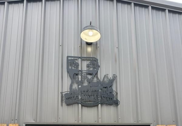 Cut metal Break Time Ranch sign mounted on the lodge exterior beneath a gooseneck barn light